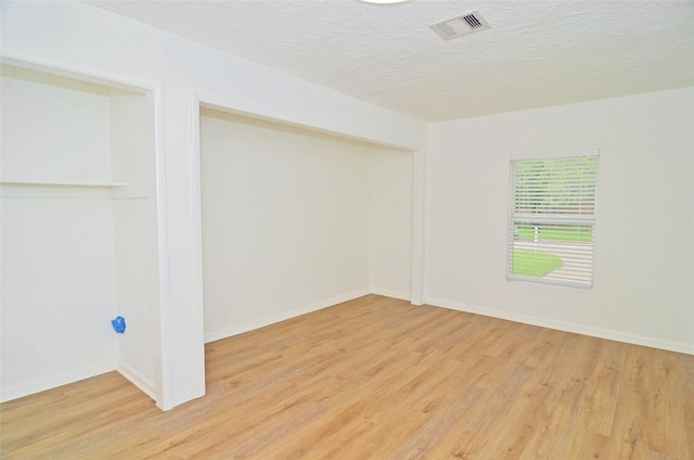 empty room with a textured ceiling and light hardwood / wood-style floors