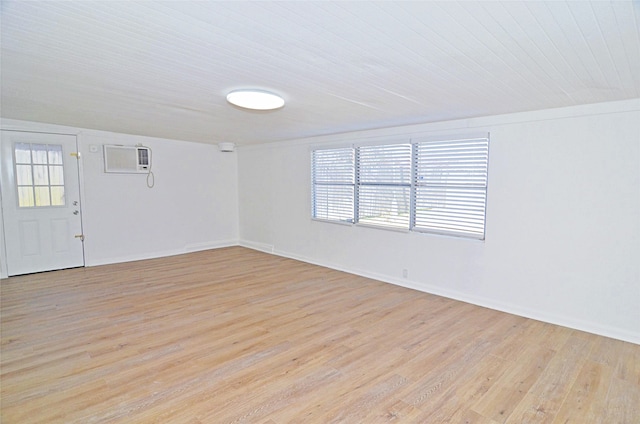 empty room featuring a wall mounted air conditioner, light hardwood / wood-style flooring, and a healthy amount of sunlight