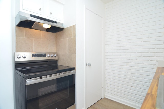 kitchen with brick wall, butcher block countertops, white cabinets, light hardwood / wood-style floors, and stainless steel electric range