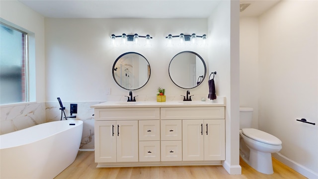 bathroom with a washtub, dual vanity, wood-type flooring, and toilet