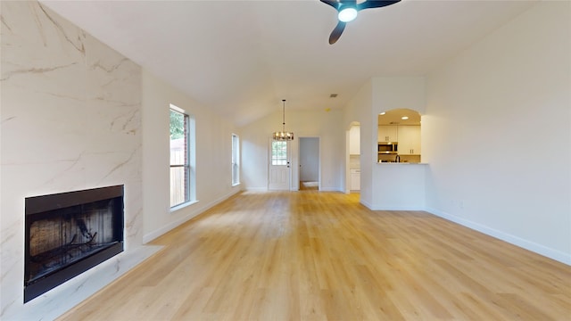 unfurnished living room with light hardwood / wood-style floors, ceiling fan with notable chandelier, lofted ceiling, and a high end fireplace