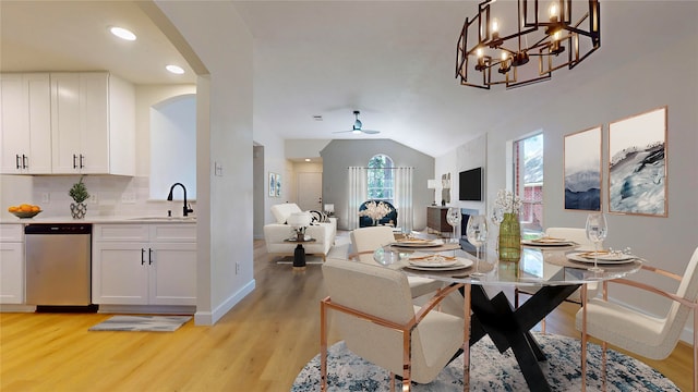 dining area with sink, ceiling fan with notable chandelier, lofted ceiling, and light wood-type flooring