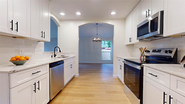 kitchen with backsplash, light hardwood / wood-style floors, appliances with stainless steel finishes, decorative light fixtures, and sink