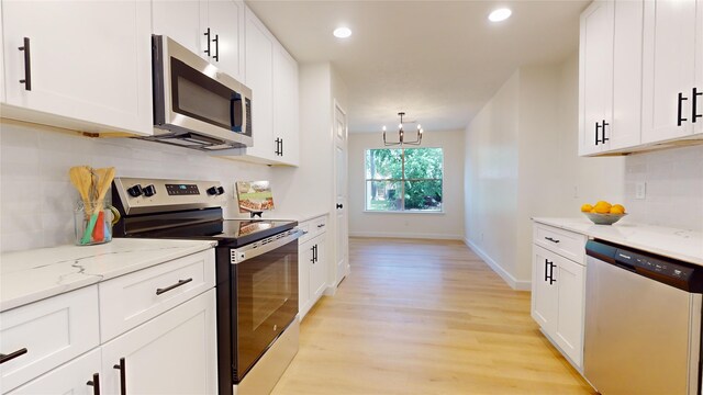 kitchen with tasteful backsplash, stainless steel appliances, white cabinets, light stone counters, and light hardwood / wood-style floors