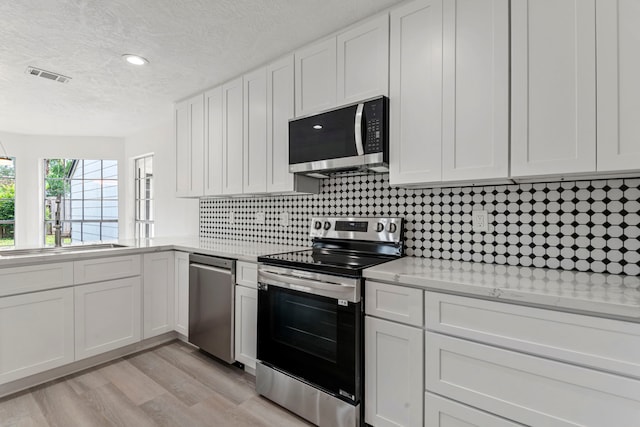 kitchen featuring white cabinetry, backsplash, light stone counters, and stainless steel appliances