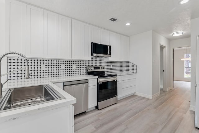 kitchen featuring backsplash, stainless steel appliances, light wood-type flooring, and white cabinets