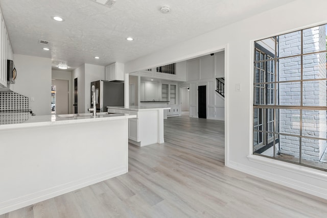 kitchen with a center island, a textured ceiling, light hardwood / wood-style flooring, appliances with stainless steel finishes, and white cabinets