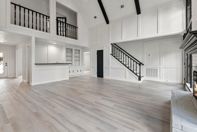 unfurnished living room featuring high vaulted ceiling, built in features, beamed ceiling, and light wood-type flooring