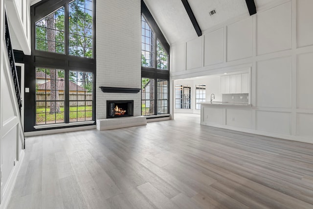 unfurnished living room with high vaulted ceiling, a fireplace, beamed ceiling, a textured ceiling, and light hardwood / wood-style flooring