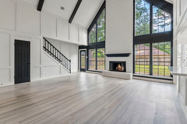 unfurnished living room with beamed ceiling, a fireplace, light hardwood / wood-style floors, and high vaulted ceiling