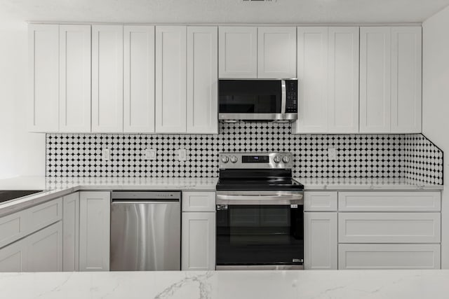 kitchen with stainless steel appliances, light stone countertops, white cabinets, and backsplash