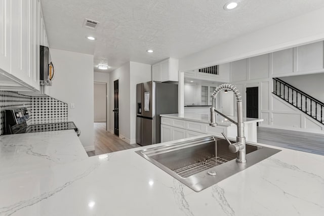 kitchen with stainless steel appliances, light stone countertops, sink, and white cabinets