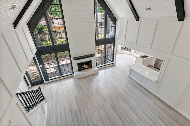 unfurnished living room featuring beam ceiling, light hardwood / wood-style floors, a brick fireplace, and a textured ceiling