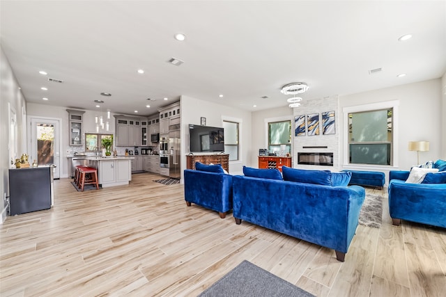 living room featuring sink, light wood-type flooring, and a large fireplace