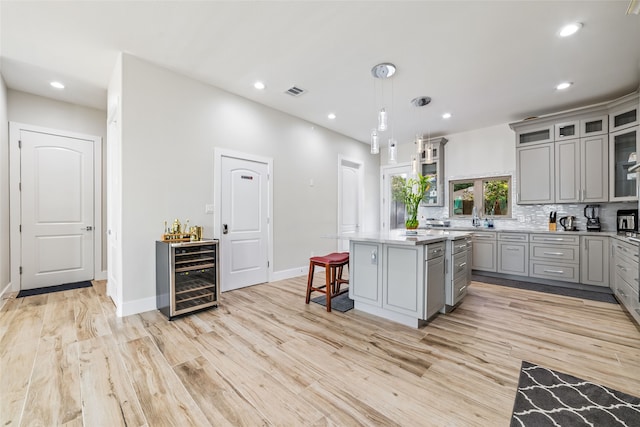 kitchen with wine cooler, a center island, light hardwood / wood-style floors, decorative light fixtures, and gray cabinetry