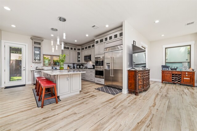 kitchen with tasteful backsplash, pendant lighting, a kitchen island, light hardwood / wood-style floors, and appliances with stainless steel finishes