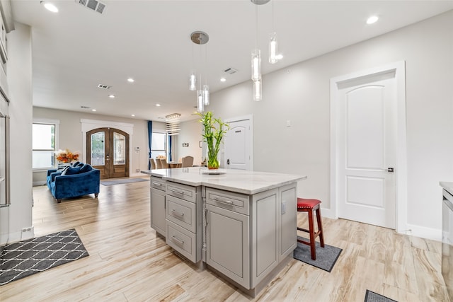 kitchen featuring a kitchen island, light hardwood / wood-style floors, light stone countertops, a kitchen breakfast bar, and decorative light fixtures