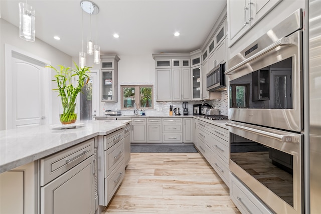 kitchen with appliances with stainless steel finishes, tasteful backsplash, pendant lighting, light hardwood / wood-style floors, and light stone countertops