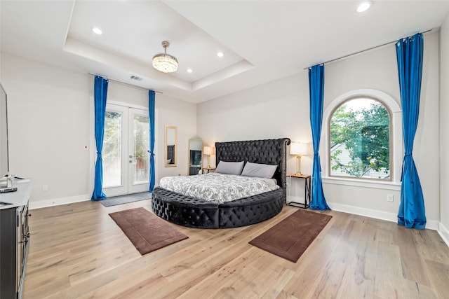 bedroom with a raised ceiling, access to outside, french doors, and hardwood / wood-style floors