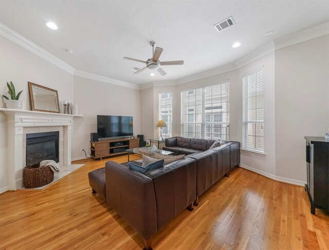 living room featuring a tiled fireplace, light wood-type flooring, ornamental molding, and ceiling fan