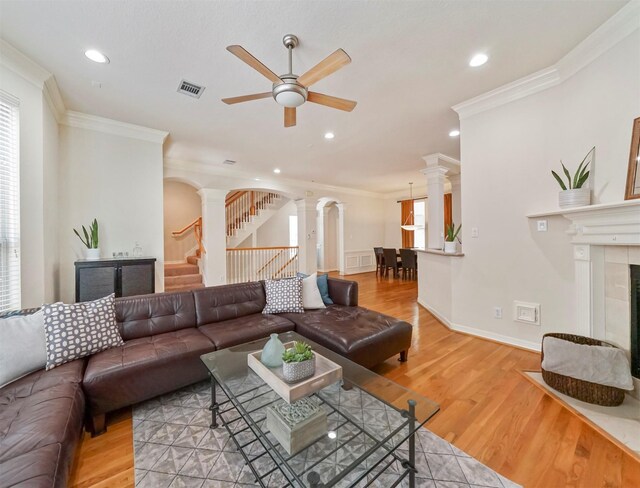 living room with decorative columns, light hardwood / wood-style flooring, a fireplace, ornamental molding, and ceiling fan