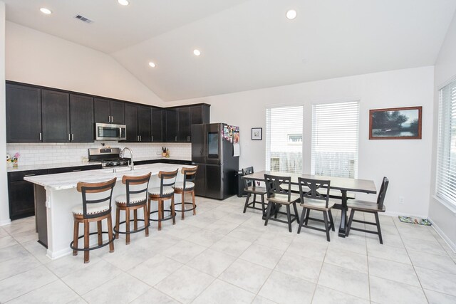 kitchen featuring vaulted ceiling, backsplash, an island with sink, and stainless steel appliances