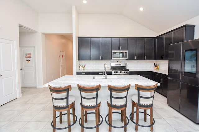 kitchen with light tile patterned floors, backsplash, an island with sink, and stainless steel appliances