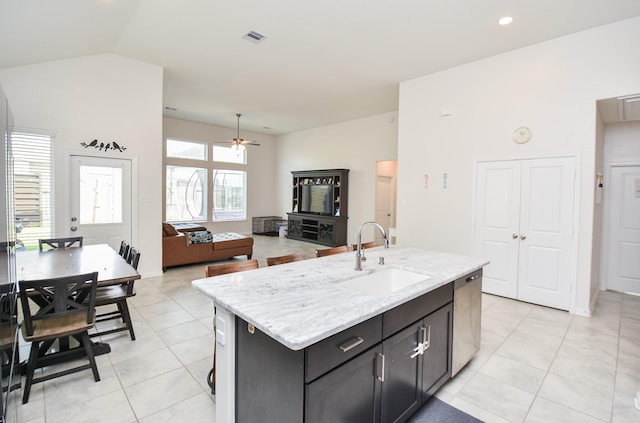 kitchen with dishwasher, sink, light stone counters, light tile patterned floors, and a center island with sink