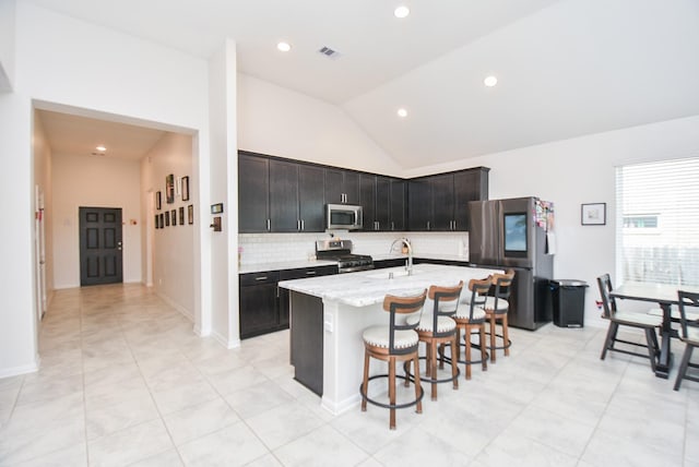 kitchen featuring a center island with sink, stainless steel appliances, tasteful backsplash, light stone countertops, and sink