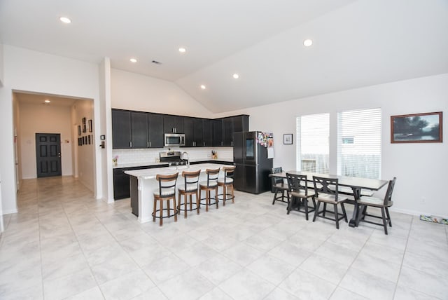 kitchen with tasteful backsplash, vaulted ceiling, a center island with sink, a kitchen bar, and stainless steel appliances