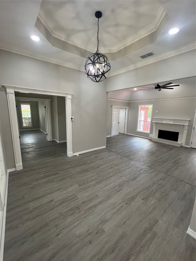 unfurnished living room featuring ceiling fan with notable chandelier, dark hardwood / wood-style floors, a tray ceiling, and ornamental molding