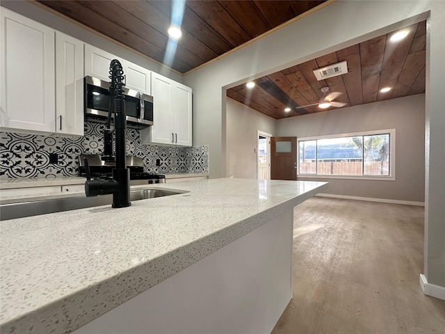 kitchen with decorative backsplash, light wood-type flooring, light stone counters, wood ceiling, and white cabinets