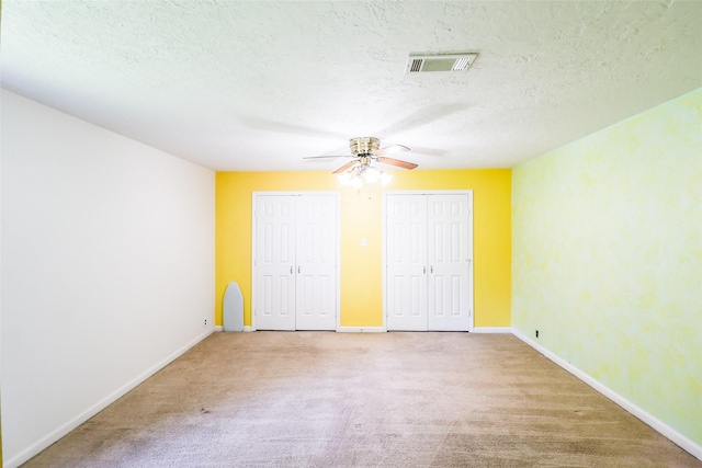 unfurnished bedroom with ceiling fan, two closets, light colored carpet, and a textured ceiling