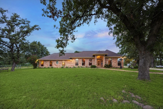 view of front facade with brick siding, fence, and a yard