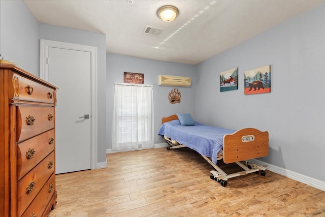 bedroom with a wall mounted AC and light wood-type flooring