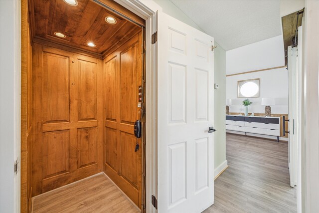 hall featuring light hardwood / wood-style flooring, elevator, and wood ceiling