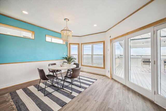 dining space with hardwood / wood-style floors, an inviting chandelier, a textured ceiling, crown molding, and a water view