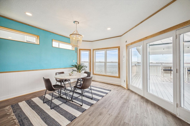 dining area featuring hardwood / wood-style flooring, ornamental molding, a chandelier, and a water view