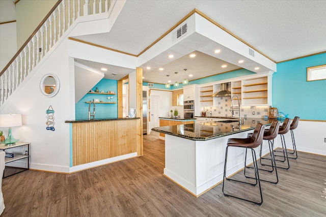 kitchen featuring wall chimney range hood, kitchen peninsula, light wood-type flooring, a textured ceiling, and tasteful backsplash