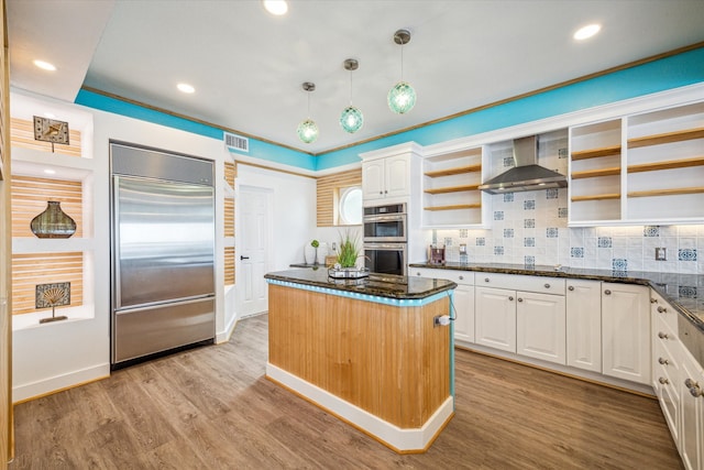 kitchen featuring wall chimney range hood, backsplash, light wood-type flooring, white cabinetry, and appliances with stainless steel finishes