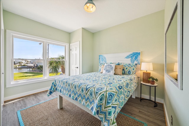 bedroom with a water view and dark hardwood / wood-style flooring