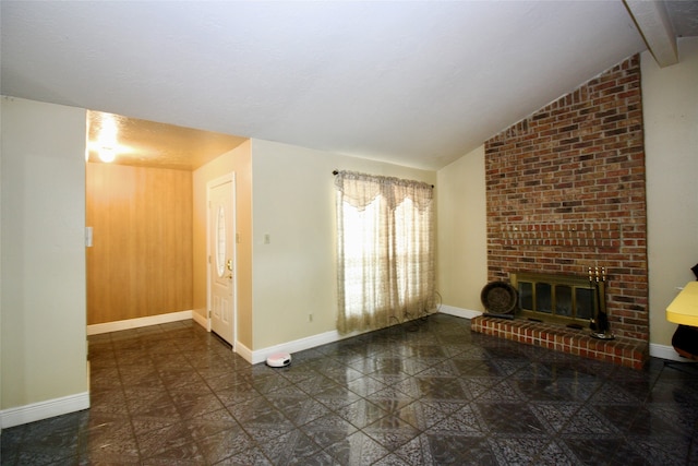 unfurnished living room with a fireplace, lofted ceiling with beams, brick wall, and dark tile patterned flooring