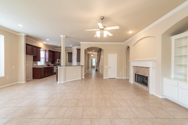 unfurnished living room featuring baseboards, a ceiling fan, a tile fireplace, ornamental molding, and built in shelves