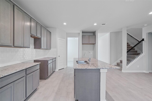 kitchen with light stone countertops, gray cabinetry, sink, light hardwood / wood-style floors, and an island with sink