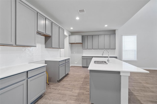 kitchen featuring an island with sink, light hardwood / wood-style flooring, gray cabinetry, and sink