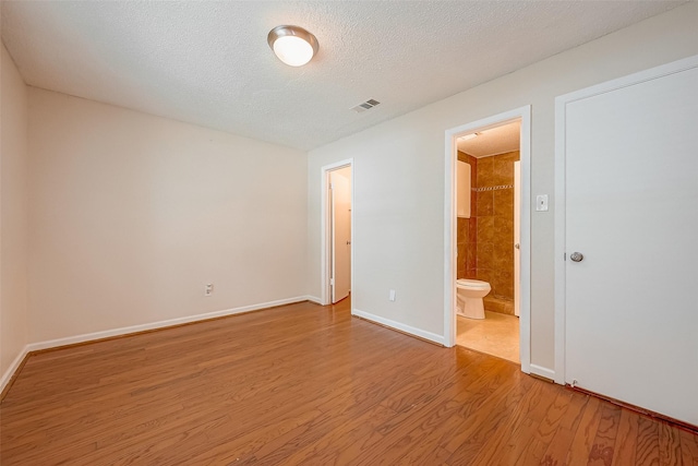 unfurnished bedroom featuring light wood-type flooring, ensuite bathroom, and a textured ceiling