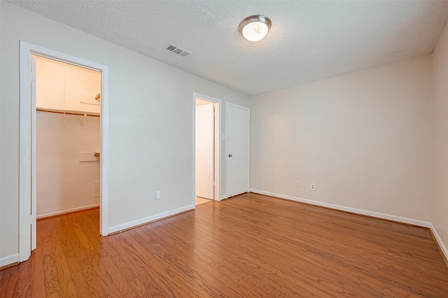 unfurnished bedroom featuring a spacious closet, a closet, a textured ceiling, and light hardwood / wood-style flooring