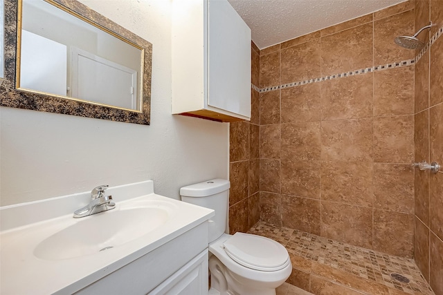 bathroom featuring a textured ceiling, toilet, vanity, and tiled shower