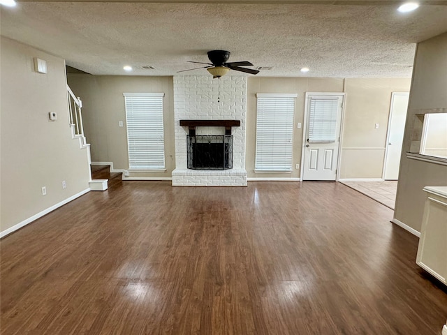 unfurnished living room with a fireplace, ceiling fan, dark wood-type flooring, and a textured ceiling