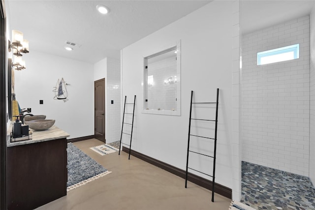 bathroom with concrete flooring, a tile shower, and vanity